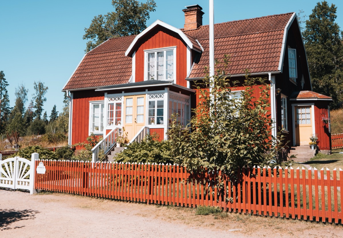 Rött trähus med vita spröjsade fönster och rött staket i Småland