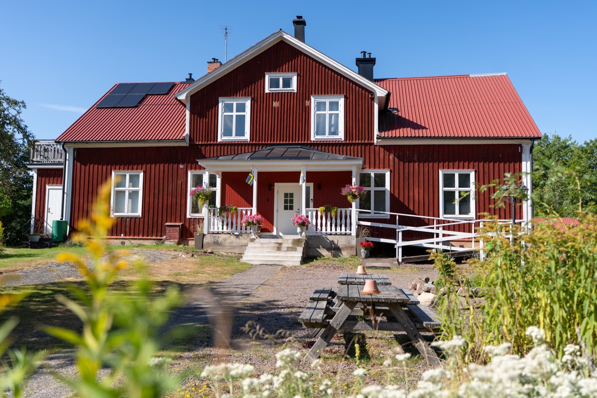 Det röda huvudhuset med vit veranda och blomlådor på sommaren